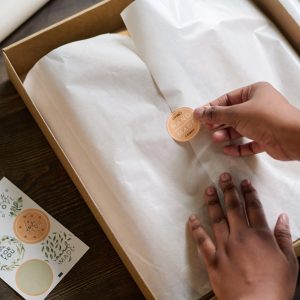 Hands of female worker of warehouse putting sticker on top of wrapping paper