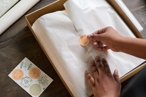 Hands of female worker of warehouse putting sticker on top of wrapping paper