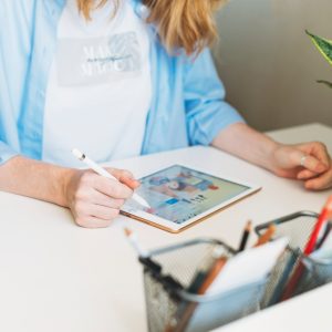 Young woman with red hair illustrator web designer draws on tablet at desk at the home office