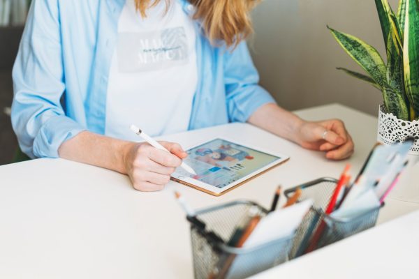 Young woman with red hair illustrator web designer draws on tablet at desk at the home office